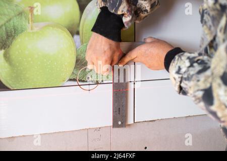 A man using a laser level and a ruler makes markings for the opening of an electrical outlet. Stock Photo