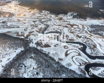 Winter aerial rural view on snowy river valley. Zmiyevsky region on Siverskyi Donets River in Ukraine from drone. Contrast black river curve in snow w Stock Photo