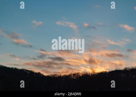 Dramatic sunset sky clouds above trees silhouette background. Evening vivid colored cloudy blue countryside view Stock Photo