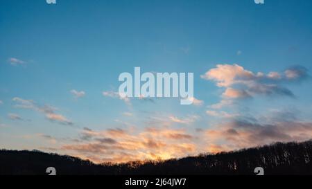 Epic sunset sky cloudscape above trees silhouette background. Evening vivid colored cloudy blue countryside view Stock Photo