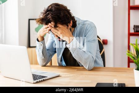 Stressed man with laptop sitting on desk at home office Stock Photo
