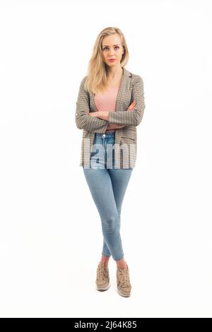 nice Cucasian blonde girl standing with arms crossed and looking into the camera seriously wearing sneakers denim jacket and pink shirt studio shot full shot white background copy space. High quality photo Stock Photo