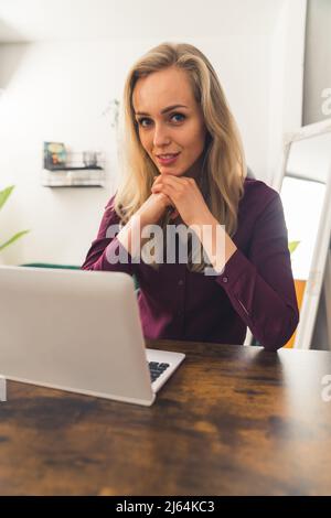 love my remote job - blonde girl sitting at the table and working from home remote job concept medum closeup living room vertical . High quality photo Stock Photo