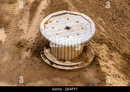 a large empty wooden reel from the cable lies on the clay soil of the construction site, selective focus Stock Photo