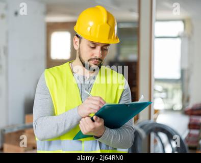 Builder making notes on indoor construction site Stock Photo