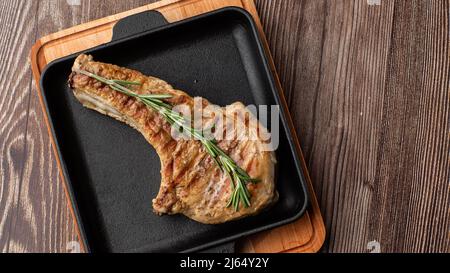 Roasted pork chop steak with spices and rosemary on black plate on wooden background. Pork, beef, chop on a bone. top view. place for text Stock Photo