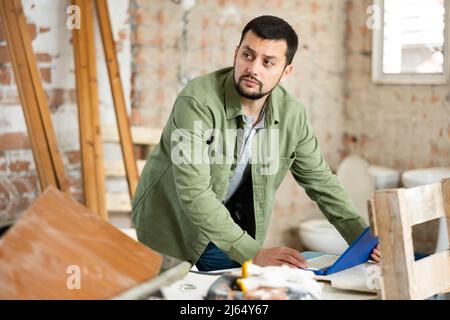 Interested young man using laptop in house during renovation Stock Photo