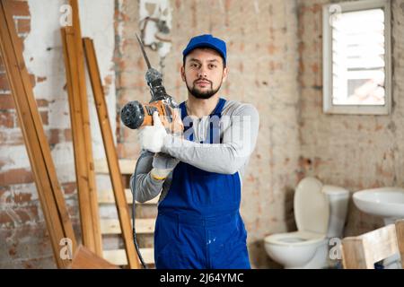 Young bearded builder holding pneumatic jackhammer in building under renovation Stock Photo