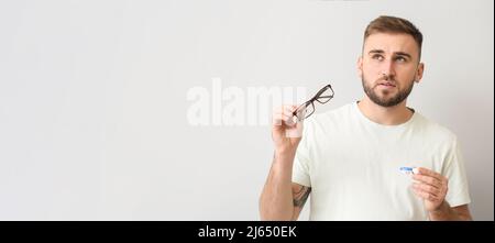 Thoughtful man choosing between contact lenses and eyeglasses on light background with space for text Stock Photo