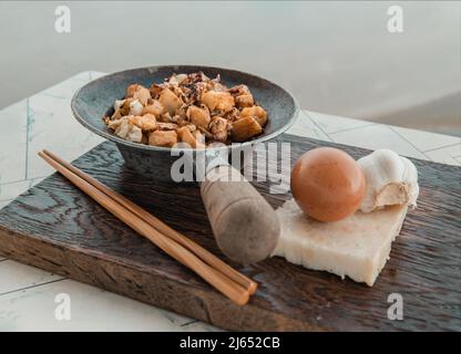 Traditional stir fried soft turnip cake or Fried radish cake (chai tow kway) in small steaming iron pot Served with wooden chopsticks on white table. Stock Photo