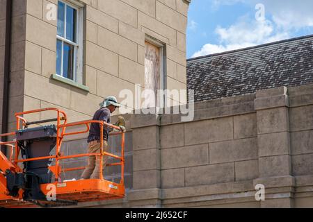 NEW ORLEANS, LA, USA - APRIL 21, 2022: Worker repairs top of historic concrete wall from an industrial lift in the French Quarter Stock Photo