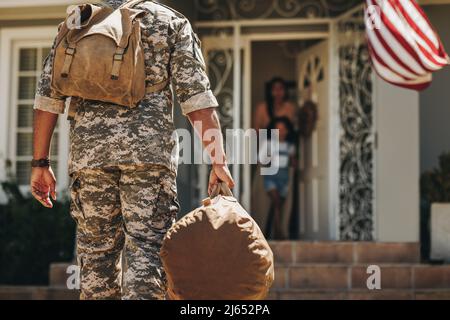 Rearview of an American soldier coming back home to his family. Serviceman surprising his wife and daughter with his return. Military man reuniting wi Stock Photo