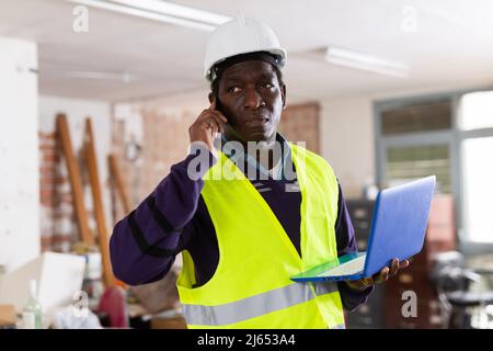 Man construction worker with laptop talking ob phone inside apartment Stock Photo