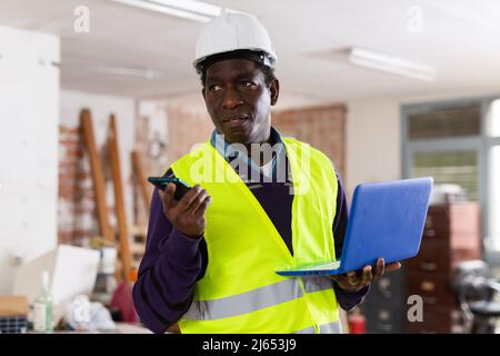 Man construction worker with laptop talking ob phone inside apartment Stock Photo