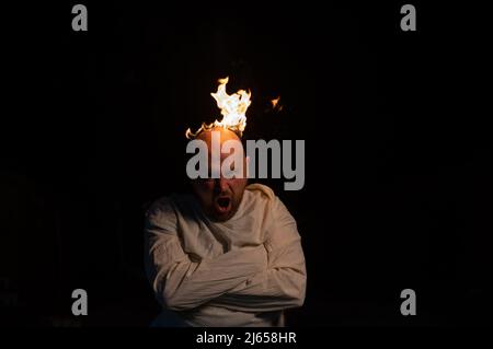 Bald man in a straitjacket with a burning head on a dark background. Stock Photo