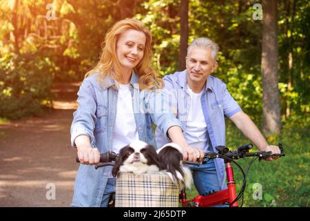 Active old age, people and lifestyle concept happy senior couple riding bicycles in summer park on a sunny day in casual comfortable clothes, enjoy life and time spent together Stock Photo