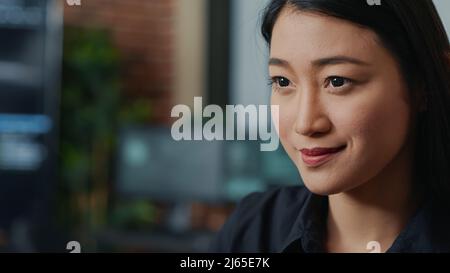Closeup portrait of focused asian coder writing online cloud computing code and smiling sitting at desk in database development agency. Friendly app developer working casually computing big data. Stock Photo
