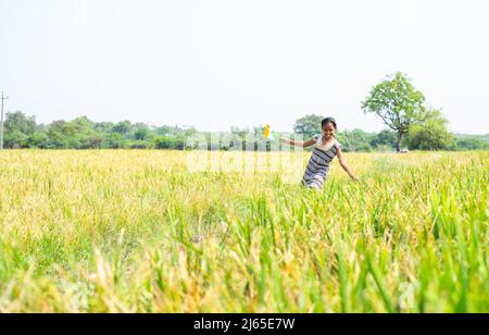 Dancing young village girl kid by holding indian flag at pady agriculture field - concept of freedom, republic or independence celebration and rural Stock Photo