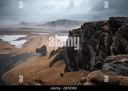 Black sand beach, moss covered cliffs and mountains of Dyrholaey, Southern Iceland, in autumn. An unrecognisable photographer is silhouetted on the cl Stock Photo