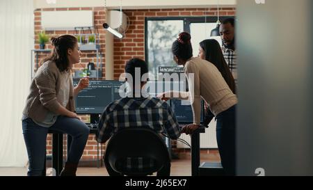 Coders discussing about source code compiling discovers errors and asks the rest of the team for explanations in front of multiple screens running algorithms. Software developers doing teamwork. Stock Photo