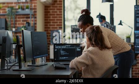 Two system engineers analyzing source code on laptop looking for errors on screen while sitting at desk. Team of app developers working on group project for ai online cloud computing project. Stock Photo