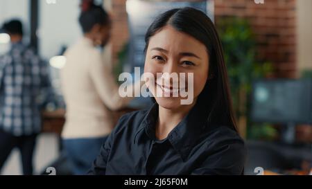 Portrait of smiling asian software developer looking at camera in cloud computing development agency. Confident programer posing happy next to colleagues working in big data office. Stock Photo