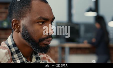 Closeup portrait of african american software developer working focused looking at computer screen while typing. System engineer writing ai code while colleagues are programming in background. Stock Photo