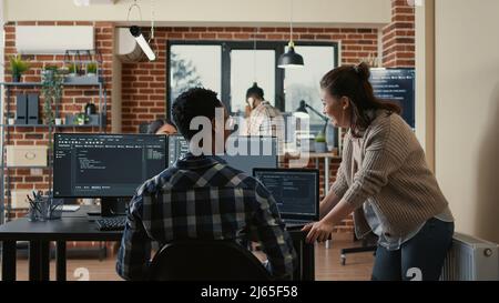 Two software developers doing high five hand gesture at desk with multiple screens running ai code celebrating successful algorithm. Programmers colleagues enjoying teamwork results in it agency. Stock Photo