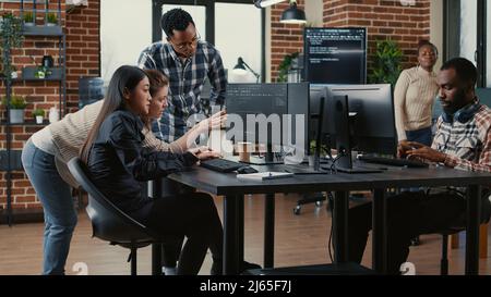 Programmers collaborating on group project compiling algorithm for new cloud computing user interface on computer screens. Mixed team of software engineers brainstorming ideas looking at running code. Stock Photo