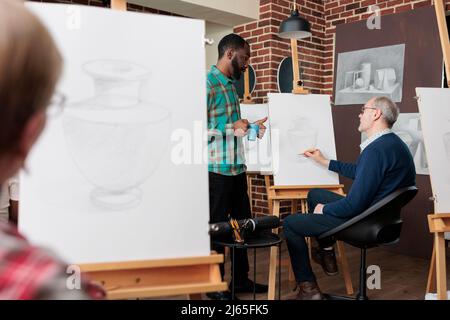 Young artist explaining drawing technique to elder person, using pencil ...