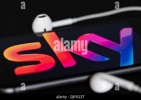 Rheinbach, Germany  28 April 2022,  The brand logo of the pay TV provider "Sky" on the display of a smartphone with headphones Stock Photo