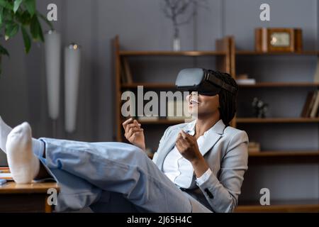 Impressed african american woman remote employee using VR headset to relax after hard working day Stock Photo