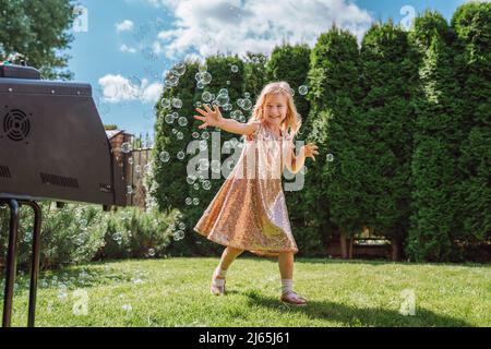 Preschool girl old enjoying soap bubbles on meadow on beautiful sunny summer day Stock Photo
