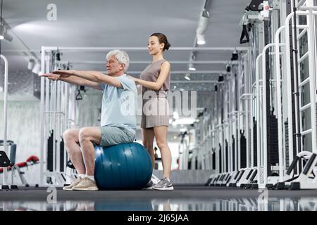 Side view portrait of young female therapist assisting senior man doing exercises in rehabilitation clinic, copy space Stock Photo