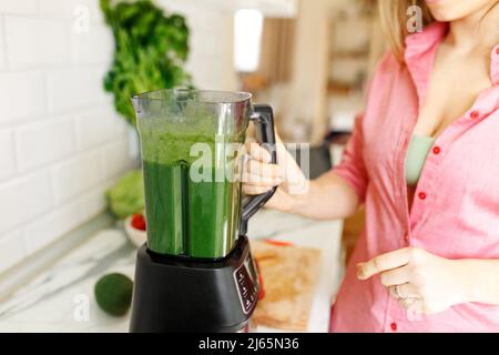 Woman preparing tasty green smoothie in kitchen.