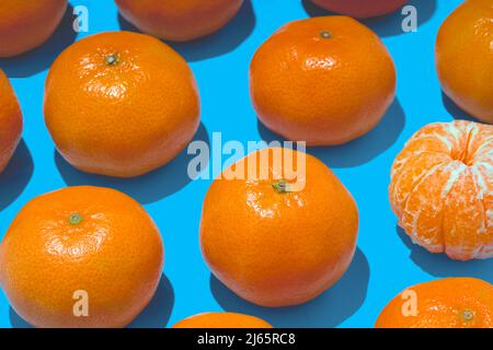 A Peeled Tangerine  Among Other Tangerines on a Light Blue Background Stock Photo