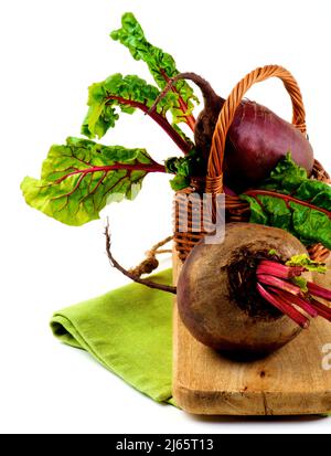 Fresh Raw Organic Beet Roots with Green Beet Tops in Wicker Basket on Napkin and Wooden Board closeup on White background Stock Photo