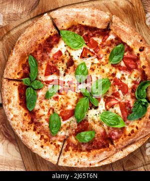 Homemade Margarita Pizza with Tomatoes, Cheese and Basil Leafs on Cutting Board closeup on Wooden background. Top View Stock Photo