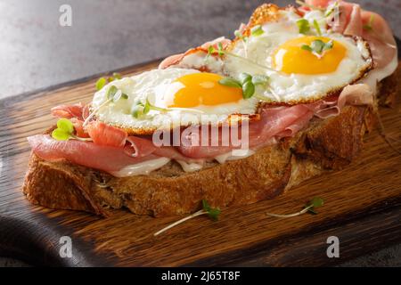 Open sandwich with cured ham and fried eggs close-up on the wooden board on the table. Horizontal Stock Photo