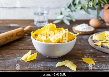 Homemade pasta Maltagliati in bowl. Basic ingredients and kitchenware backside. Rustic Italian style Stock Photo