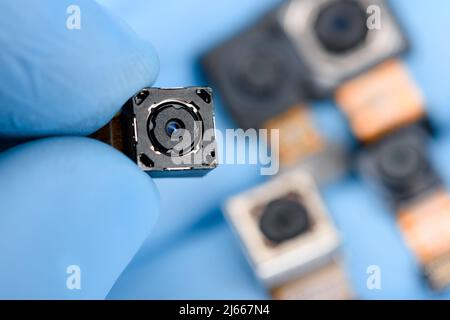 Smartphone camera module in researcher hand, with other cell phone camera sensors on background. Stock Photo