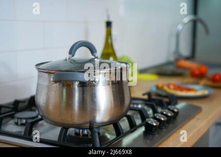 A saucepan with a glass lid is on the stove. Gas burner is on Stock Photo