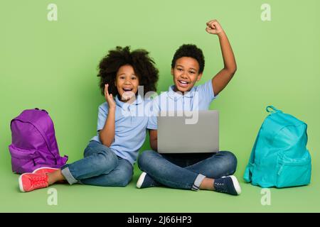 Portrait of attractive cheery pre-teen friends friendship using laptop celebrating courses lesson remote isolated on green color background Stock Photo