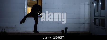 Rear View Of A Burglar Entering In A House Through A Window Stock Photo