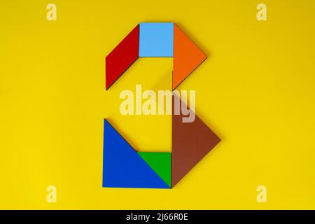 Colorful number 3 made with tangram toy, colored tangram number seven isolated on yellow background, side view of seventh numeric, kids game idea Stock Photo