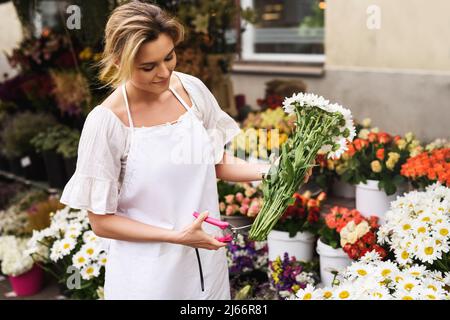 Woman florist cutting lower edge of flowers with sharp secateurs in her little flower shop Stock Photo