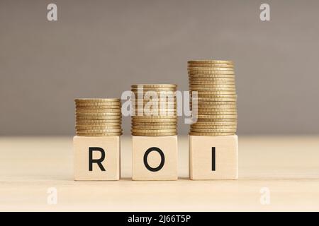 ROI word in wooden blocks with coins stacked in increasing stacks. Return on investment concept. Copy space Stock Photo