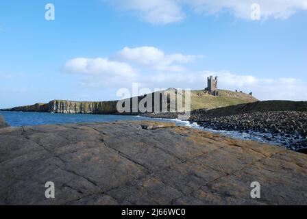 Landscape image showing Dunstanburgh Castle on its basaltic ridge seen from the rocks along the shoreline Stock Photo