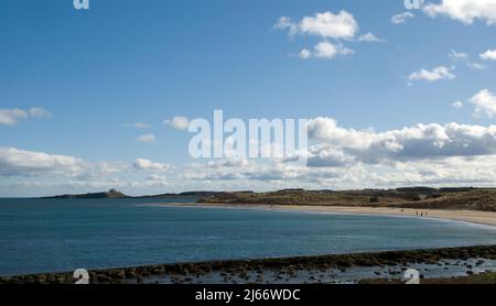 Landscape of a wide sweeping view of a curving coastline and bays towards a distant Dunstanburgh Castle on the skyline seen from Low Newton Stock Photo