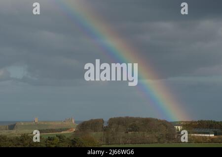 Landscape along the Northumberland coast with Dunstanburgh catle in the near distance and a large rainbow arcing over the castle in early spring Stock Photo